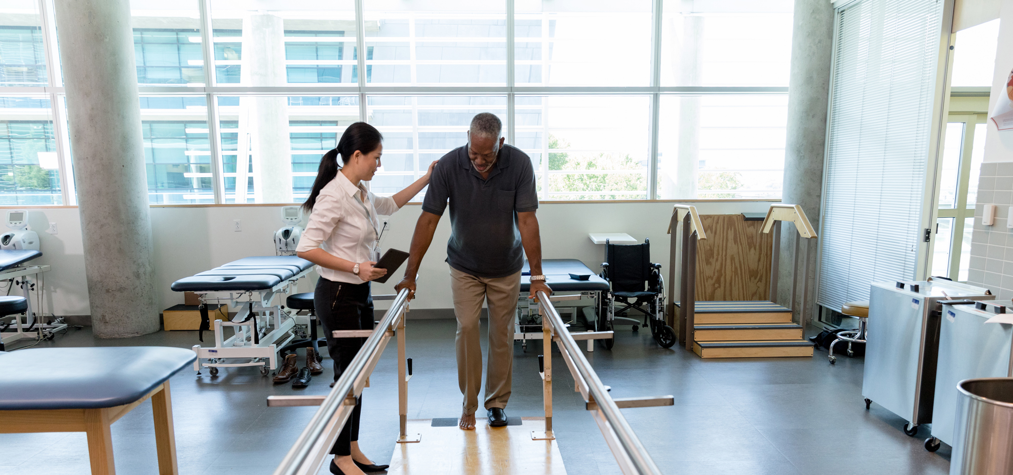 therapist helping senior man do physical therapy on balance bars